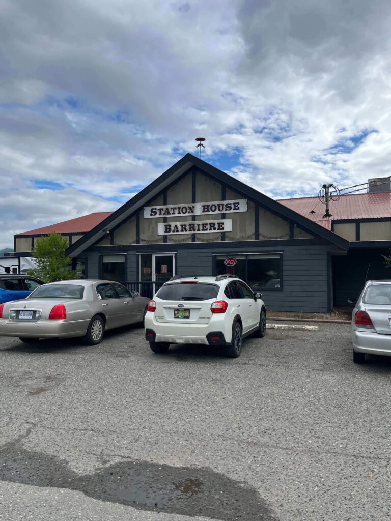 Front entrance of Station House Barriere restaurant with cars parked out front under a red roof.